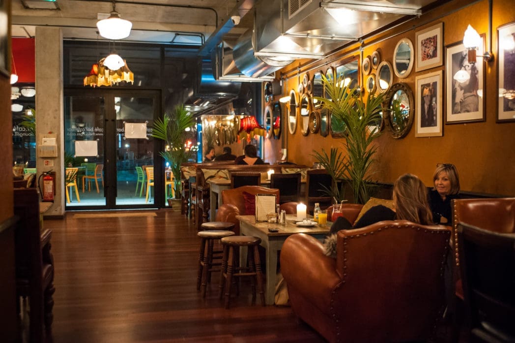 Brasco is a cozy restaurant with warm lighting, brown leather chairs, wooden floors, candles on tables, framed photos on the wall, and a few people dining and chatting.