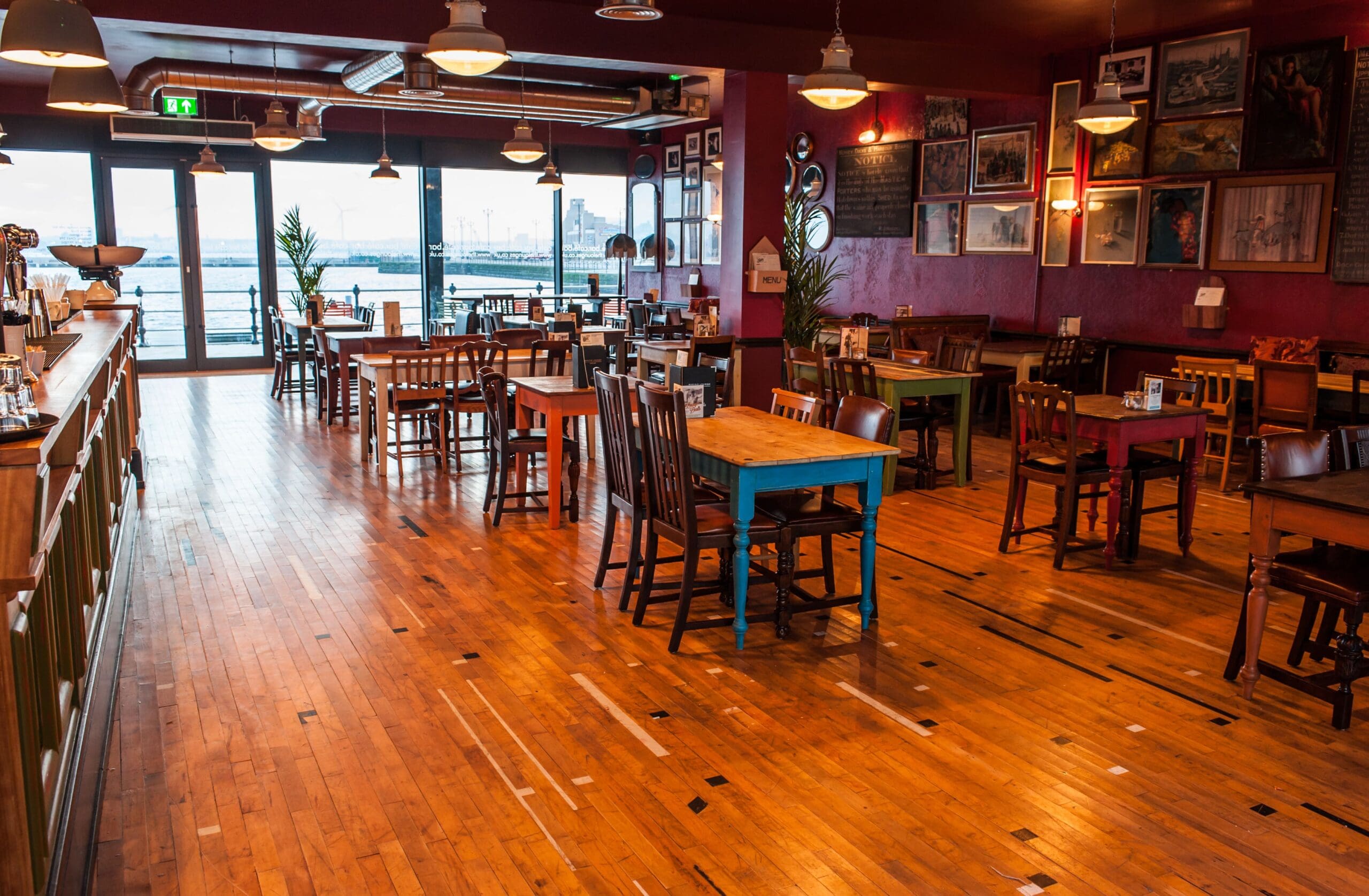 Spacious, cozy Marino restaurant with wooden floors, eclectic tables and chairs, framed art on deep red walls, and large windows offering a view of the waterfront outside.