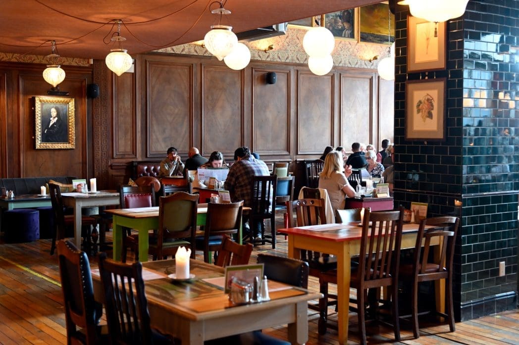 A cozy restaurant with wooden floors and mismatched tables and chairs, Caldero offers a warm, inviting atmosphere. Several groups are dining and talking beneath soft lighting and framed artwork, making every meal feel special.