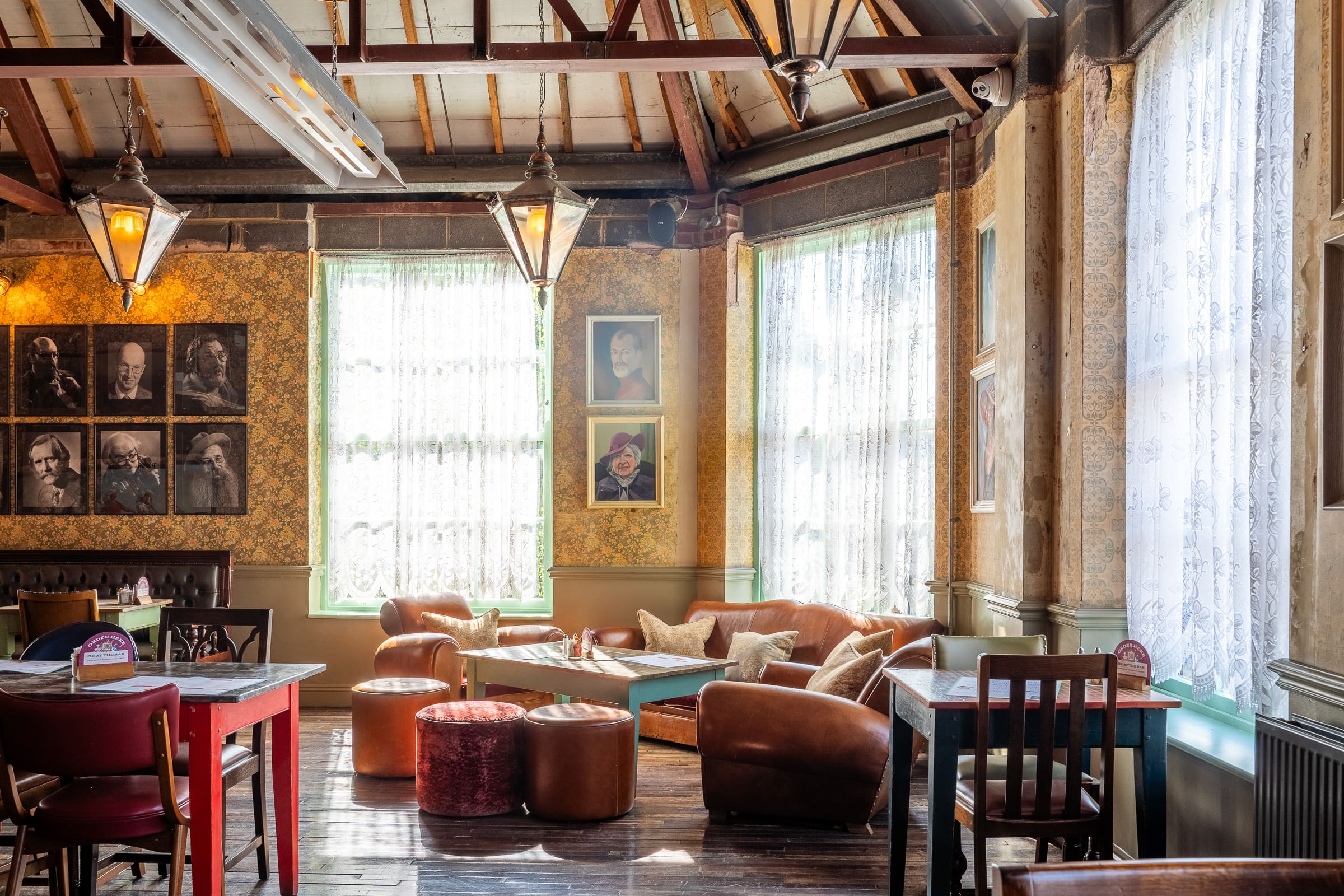 A cozy, sunlit cafe with vintage decor, leather armchairs, and small tables awaits near Castello. Lace-curtained windows and framed photos on patterned wallpaper add charm to the inviting space filled with soft natural light.