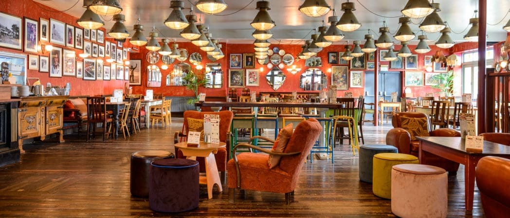 A spacious, brightly lit restaurant, Cultivo features wooden floors, eclectic chairs and tables, colorful stools, vintage decor, and framed pictures on red walls. The cozy and inviting atmosphere makes it perfect for any occasion.