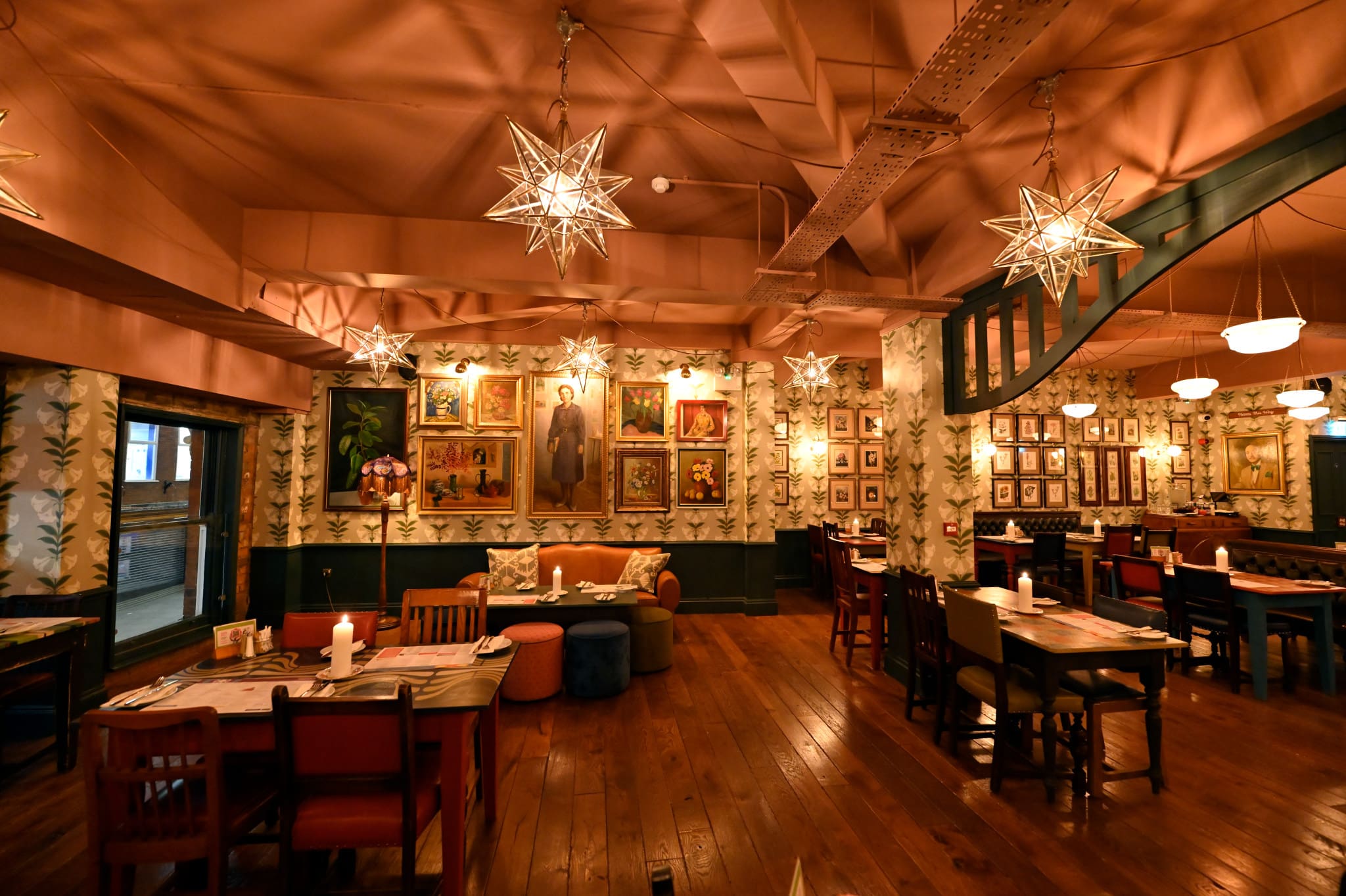A cozy restaurant with wooden floors, eclectic furniture, star-shaped pendant lights, and walls decorated with numerous framed paintings and portraits. The warm atmosphere makes Floro an inviting spot to relax and dine.