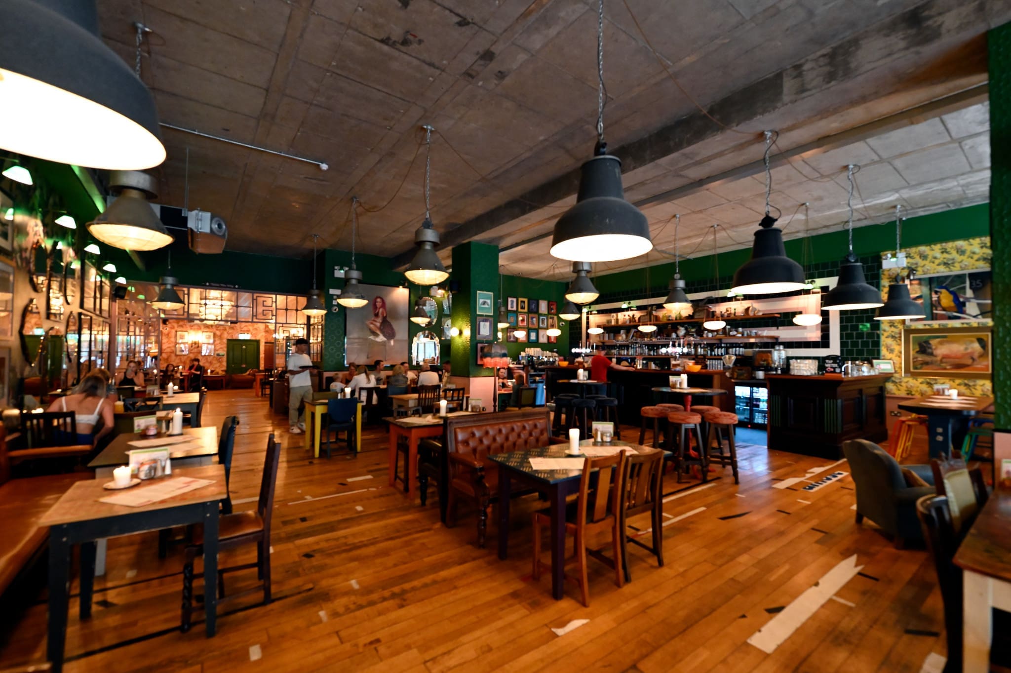 A spacious, stylish restaurant, Gallico features wooden floors, eclectic furniture, large hanging lights, and green walls adorned with framed pictures. Several tables and chairs are arranged throughout the open dining area.