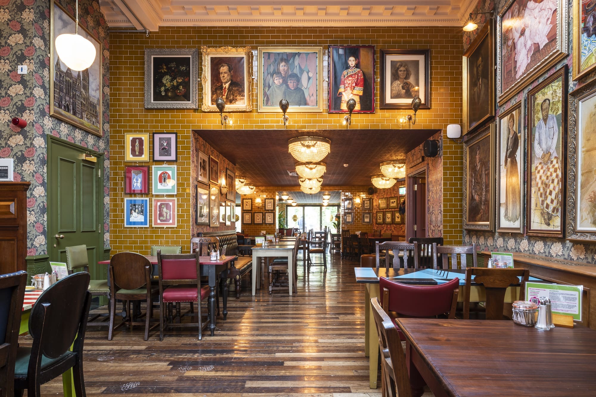 A cozy Morro restaurant with eclectic decor, wooden floors, mismatched chairs, and tables. The walls are covered with framed portraits and artwork, while warm lighting creates a welcoming atmosphere.