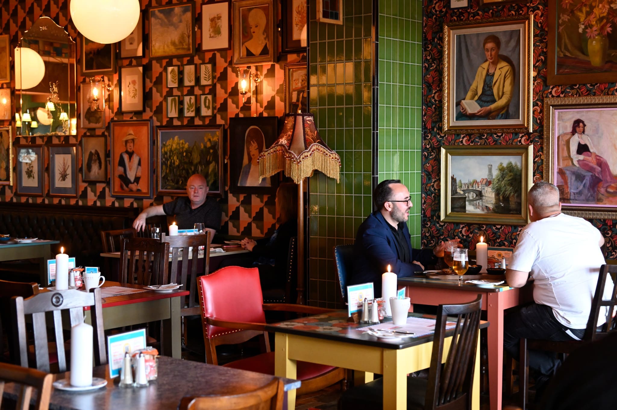 A cozy Novo restaurant with eclectic decor, featuring framed art on the walls, vintage furniture, and people sitting at tables, engaged in conversation and dining. Warm lighting adds to the inviting atmosphere.