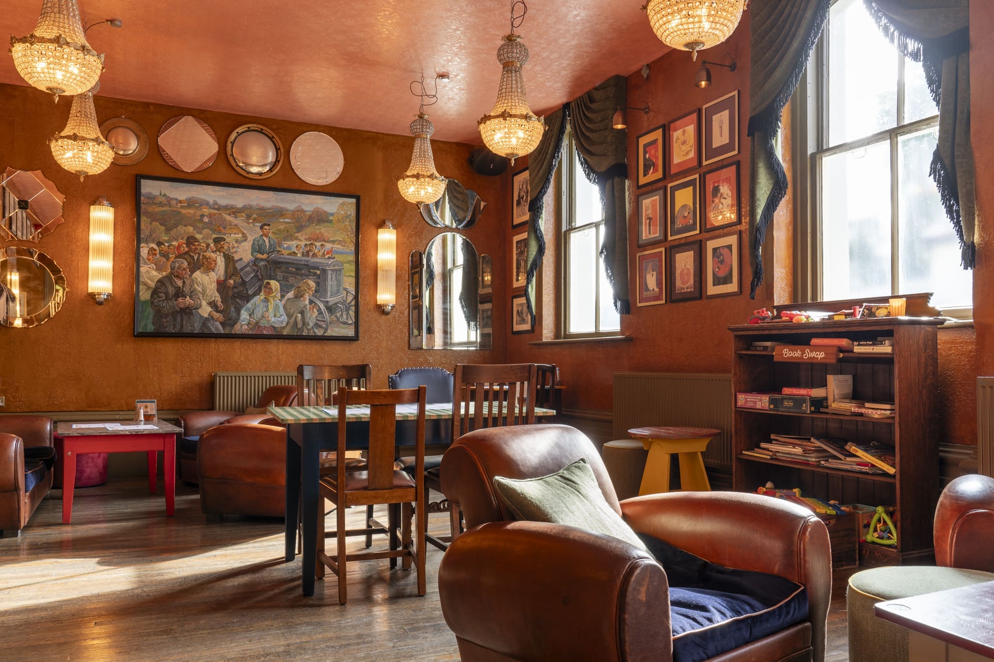 A cozy, warmly lit lounge with leather chairs, chandeliers, framed art, mirrors, and large windows. Playful touches like a children’s toy shelf and colorful decor create an eclectic atmosphere worthy of a modern Palacio.