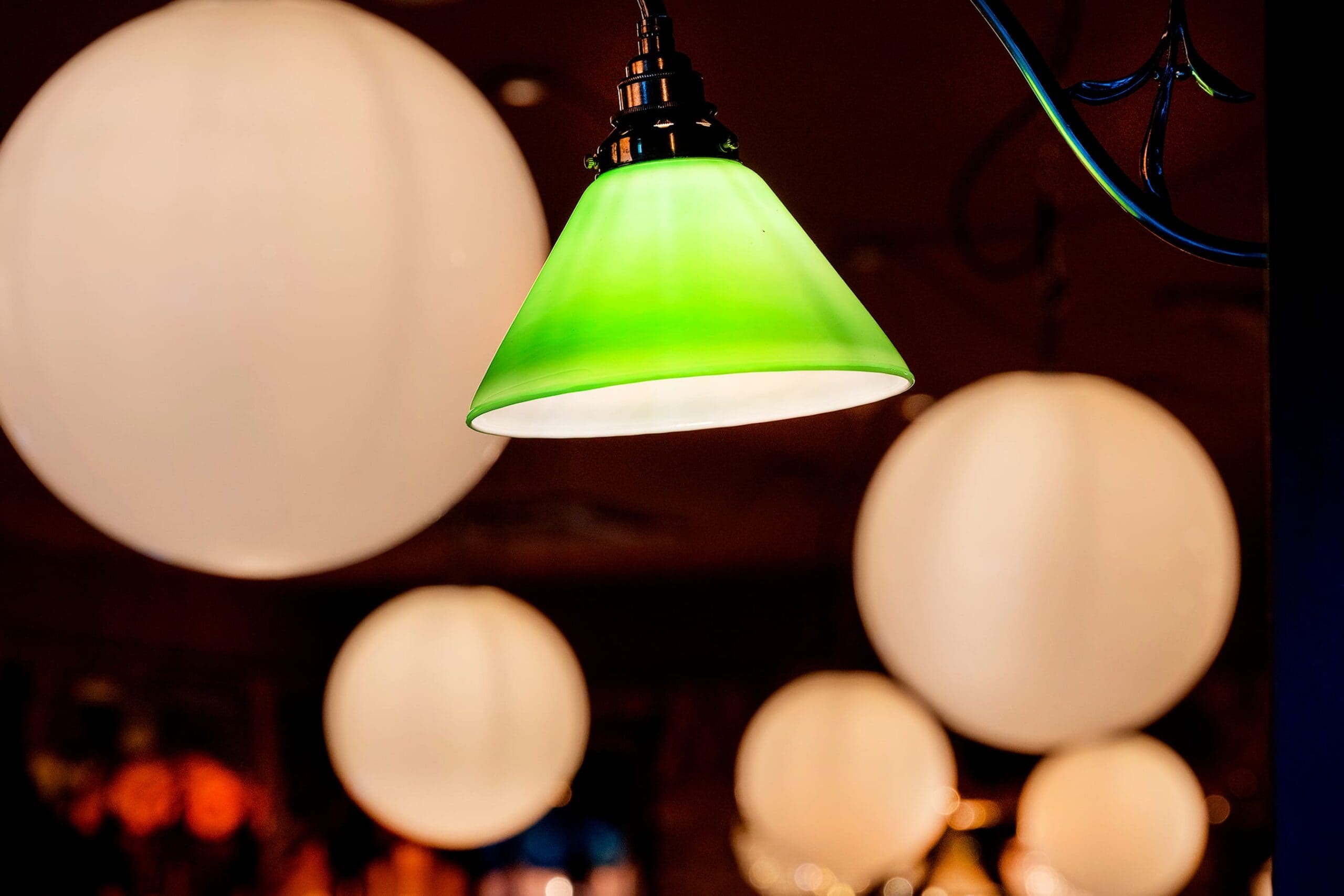 A green hanging orso lampshade is in focus, surrounded by several large, softly glowing round white lights in the blurred background.