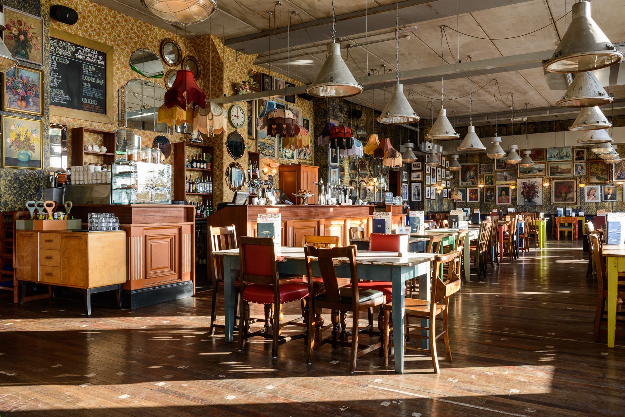 A spacious, eclectic restaurant, Visto features vintage decor, mismatched tables and chairs, framed art and clocks on the walls, pendant lights, and sunlight streaming through large windows onto the wooden floor.