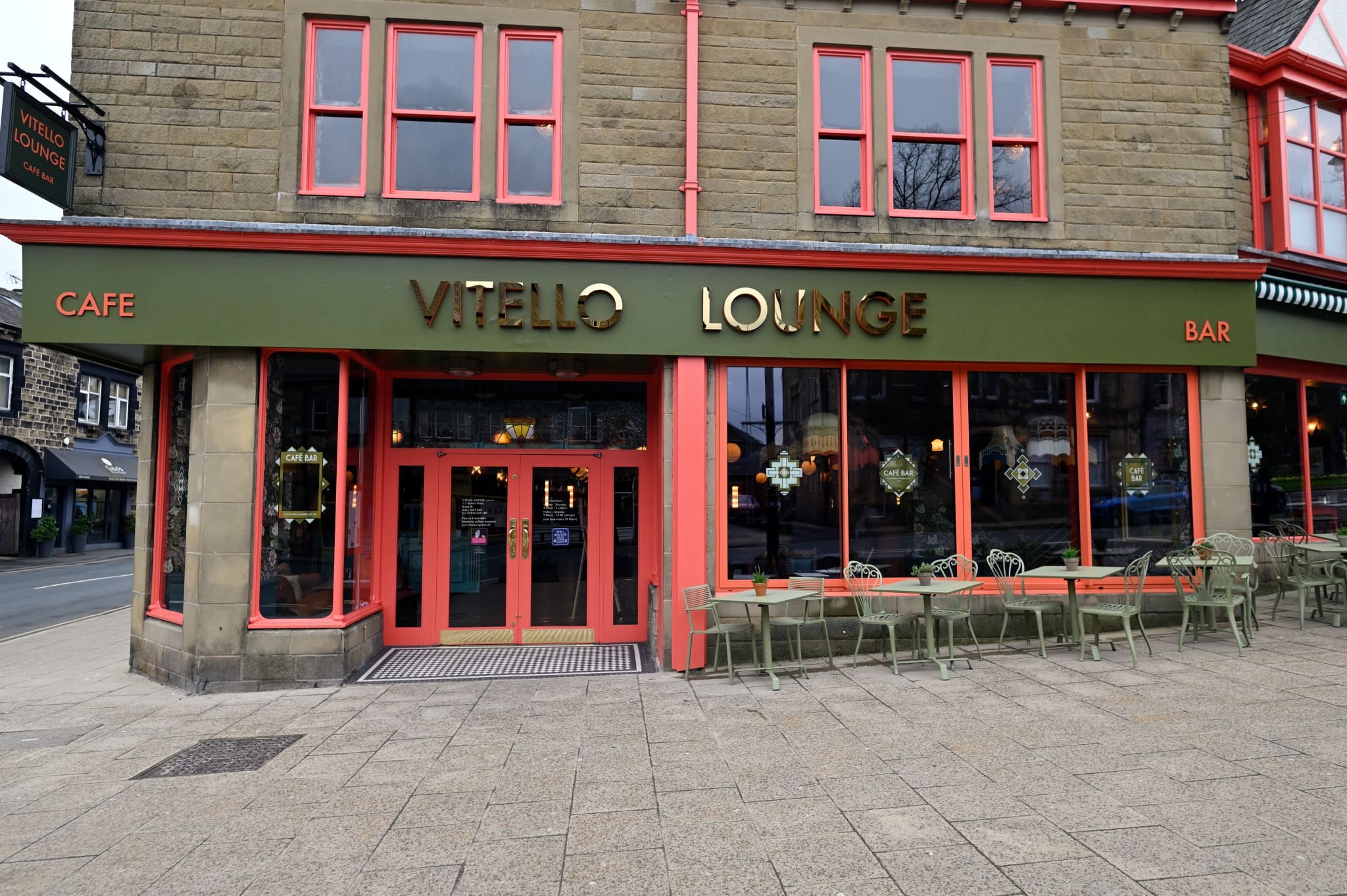 Vitello Lounge is a vibrant café bar with a green and red exterior, large windows, and outdoor seating on the paved sidewalk—perfect for watching the world go by.